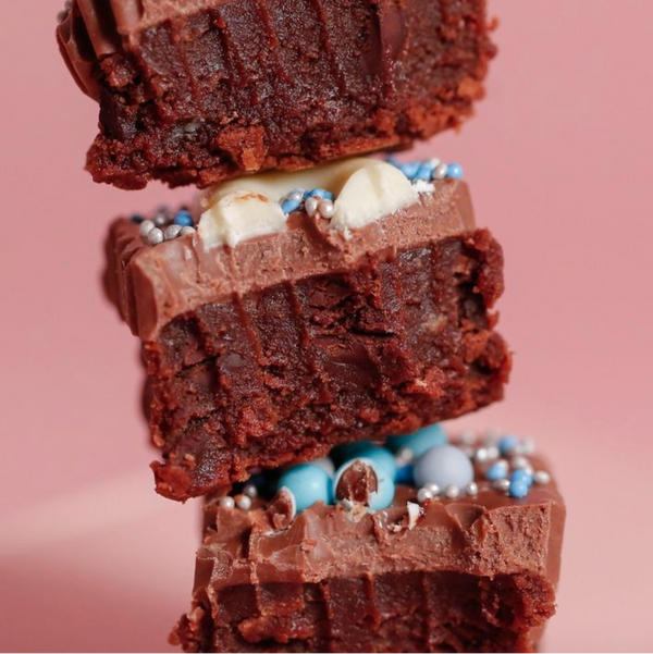 Stack of chocolate brownies with cream cheese frosting and sprinkles on a pink background.